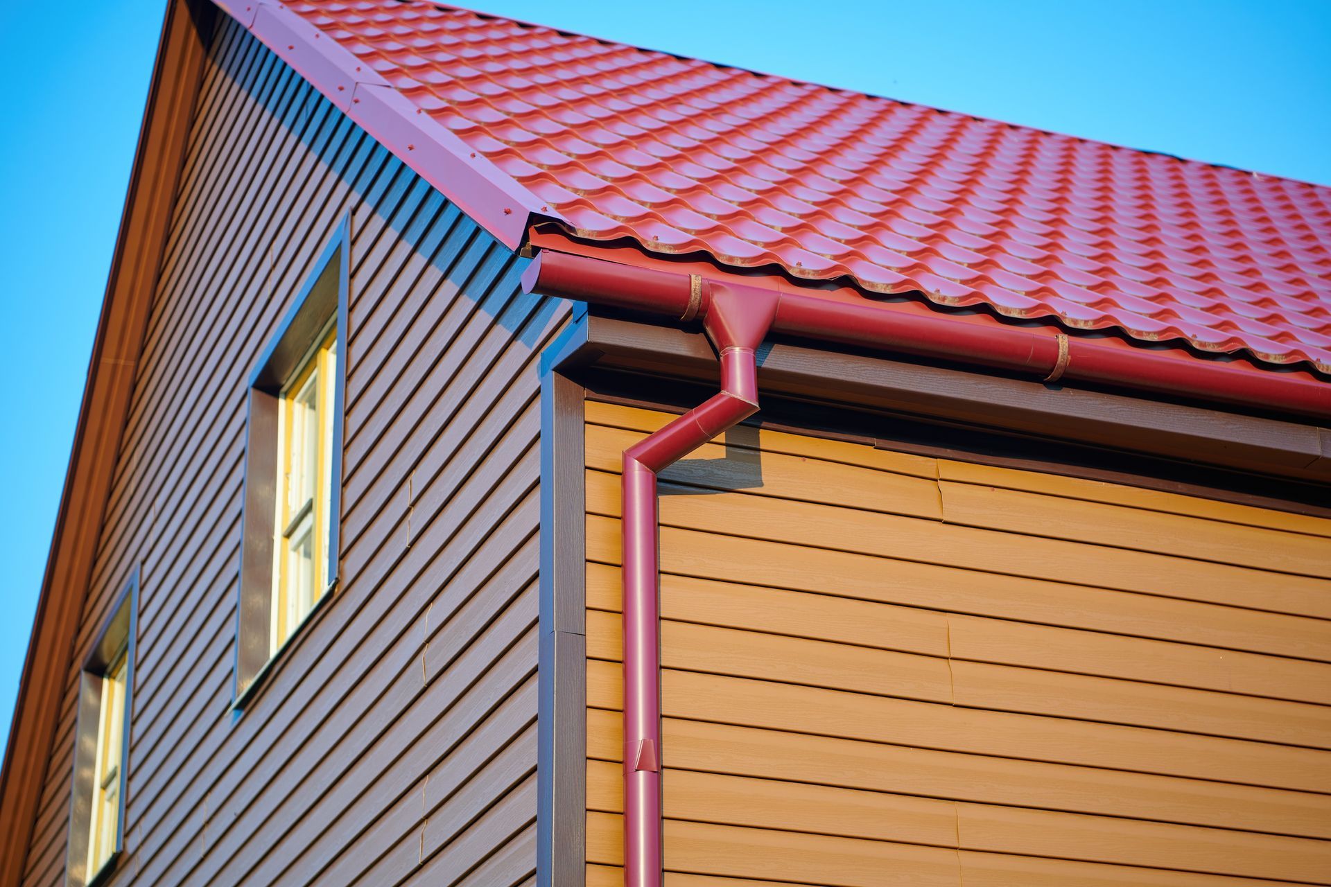 Red metal roof and gutters on a brown-sided house with two windows