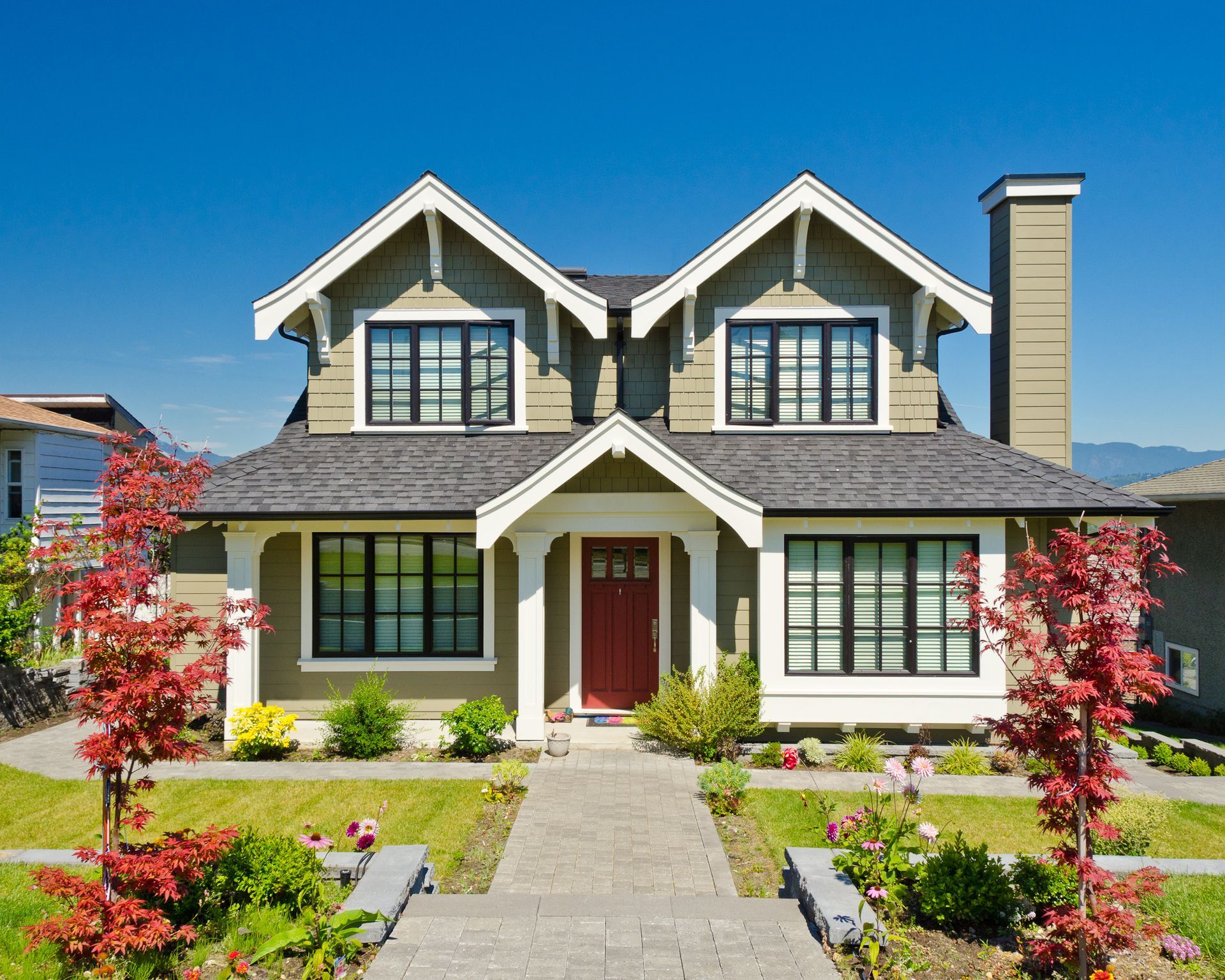 A two-story house with green siding, black-framed windows, and a red door under a blue sky.