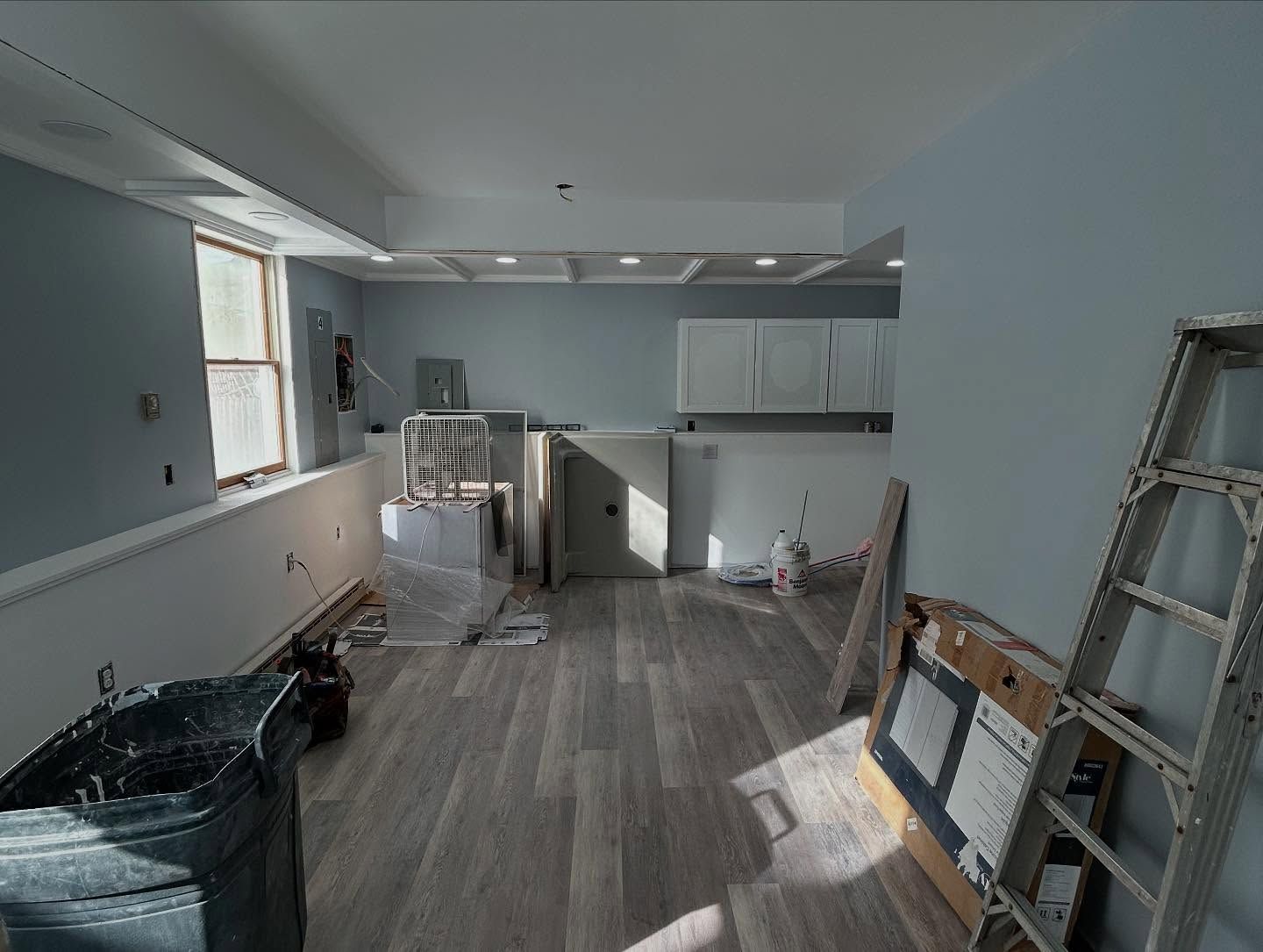 Interior renovation with light blue walls, new flooring, cabinets, ladder, and construction debris.