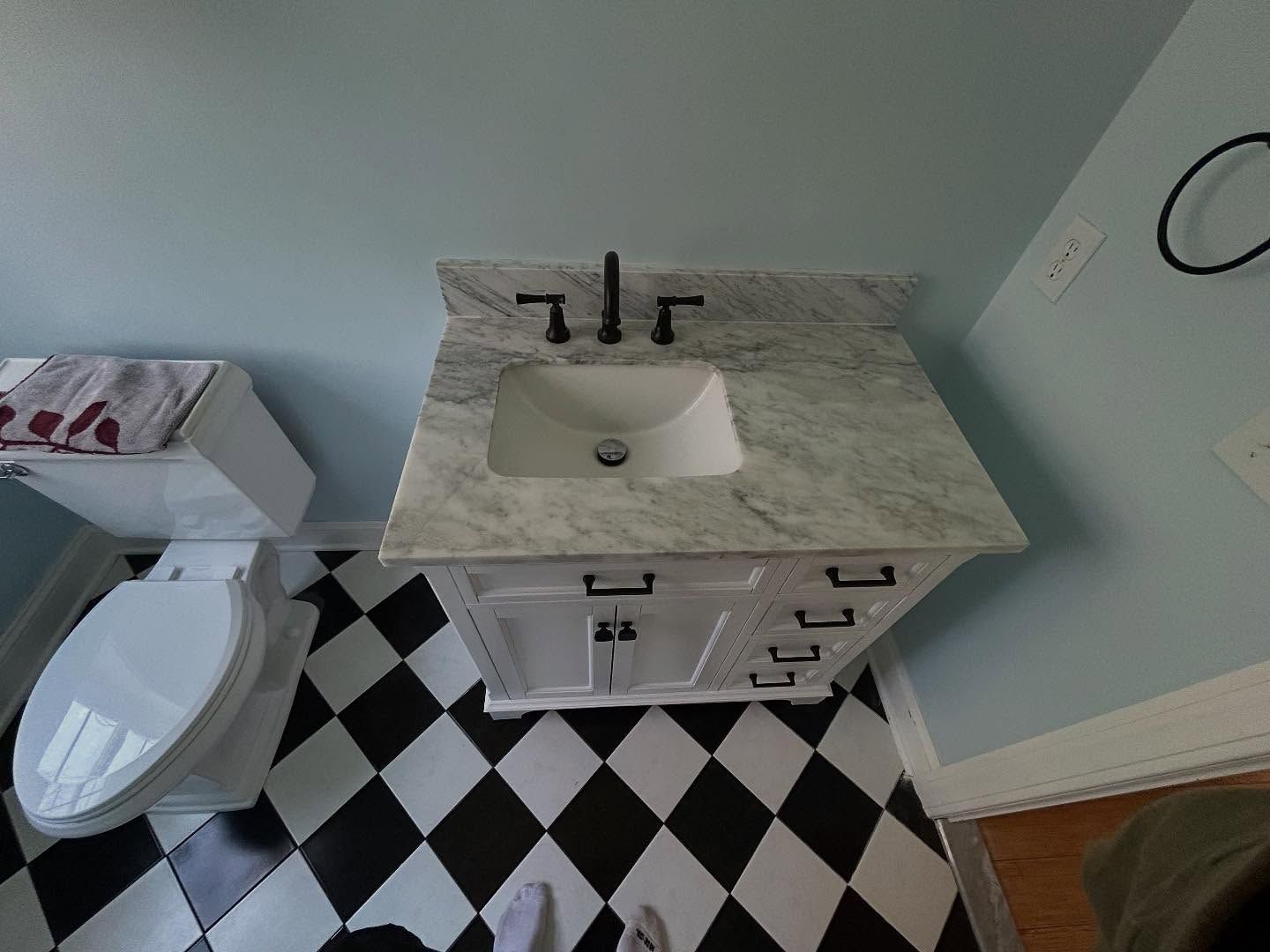 Bathroom with black and white checkered floor, white vanity with marble top, and black fixtures.