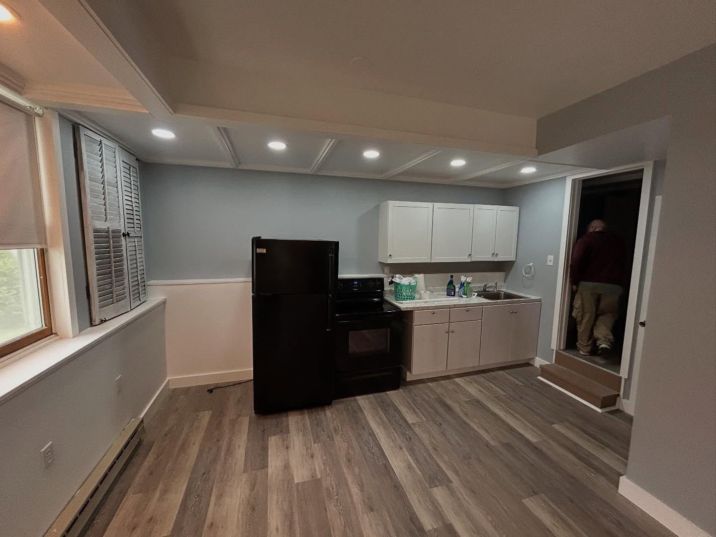 Kitchen with black appliances, white cabinets, light blue walls, and a person in the doorway.