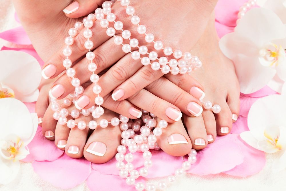 Mani e piedi con smalto rosa, adornati con gioielli di perle e circondati da fiori rosa.