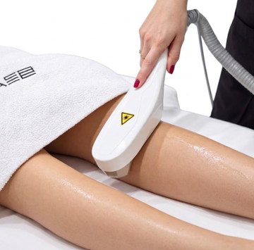 Trattamento di epilazione laser sulla gamba di una donna in una clinica, con la tecnica che indossa guanti e occhiali protettivi.