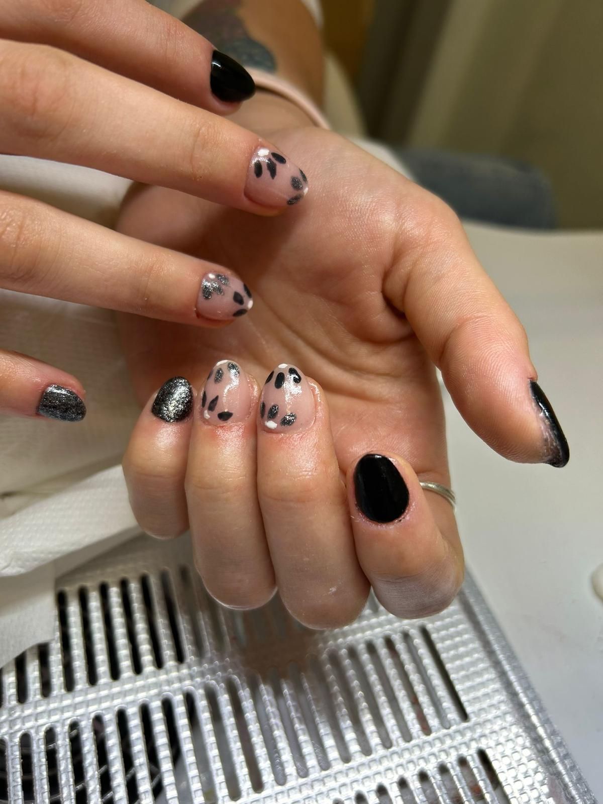 Mani con nail art nera e argento su un tavolo da manicure, una delle quali tiene in mano un telefono.