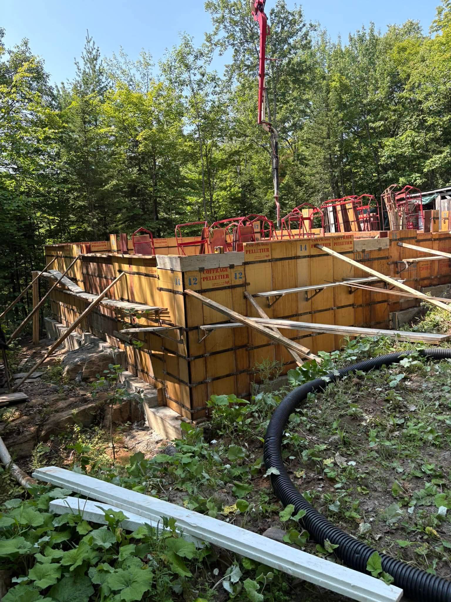 Chantier de construction avec coffrages de fondation en bois, barres d'armature rouges et arbres en arrière-plan