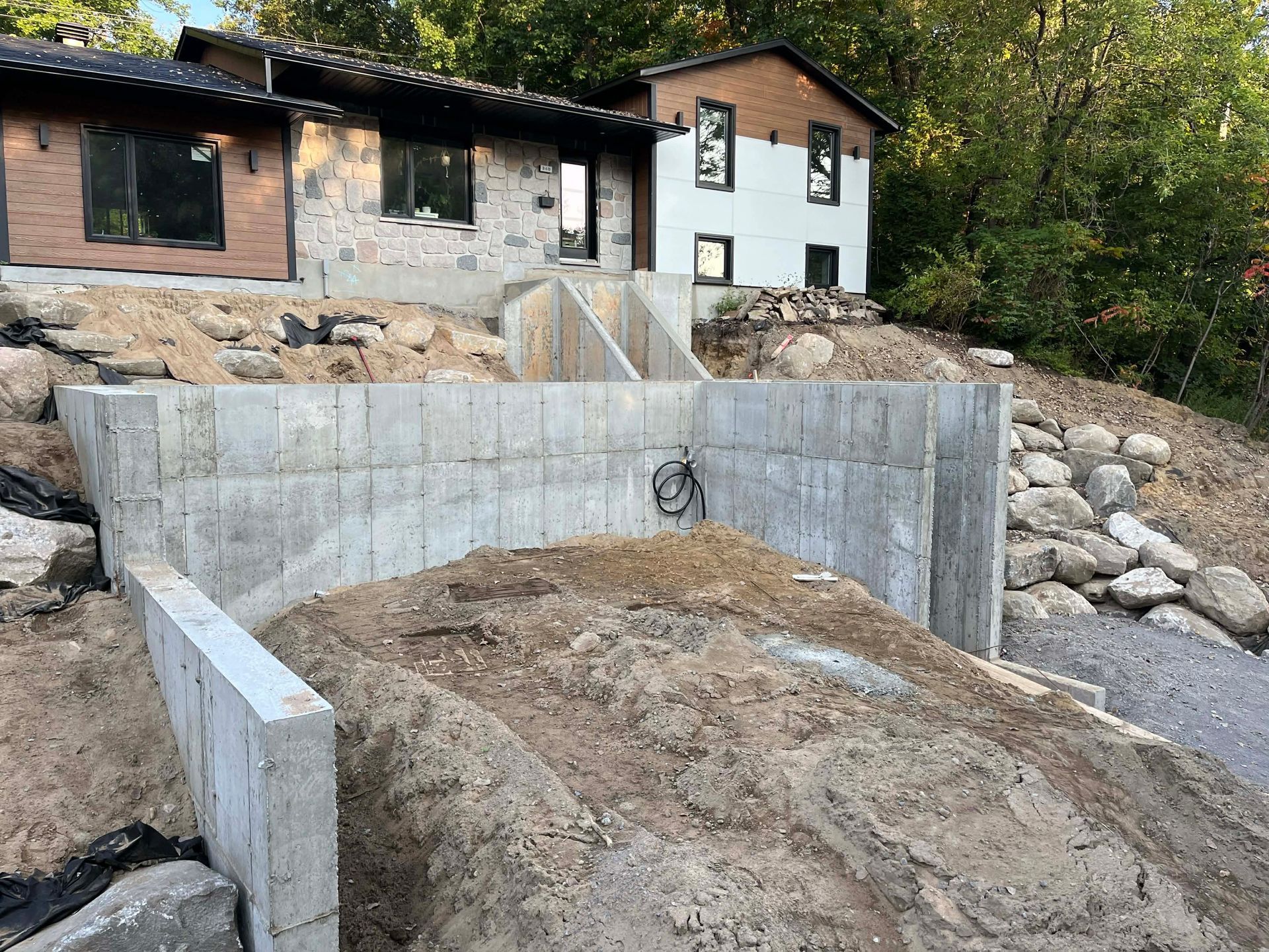 Mur de soutènement en béton et terrassement sous une maison sur un flanc de colline rocailleux.