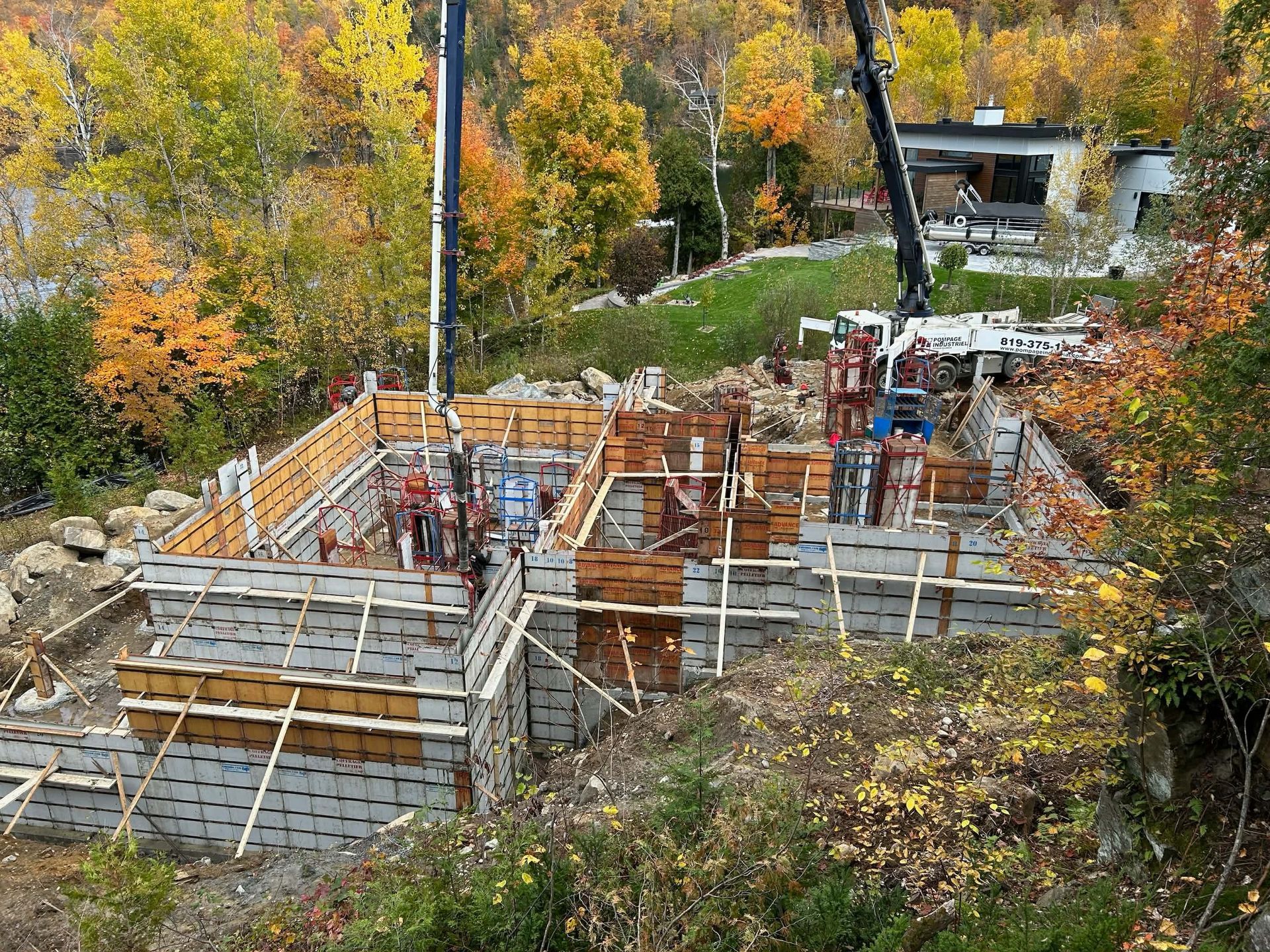 Chantier de construction avec murs de fondation en béton et ouvriers parmi les arbres d'automne