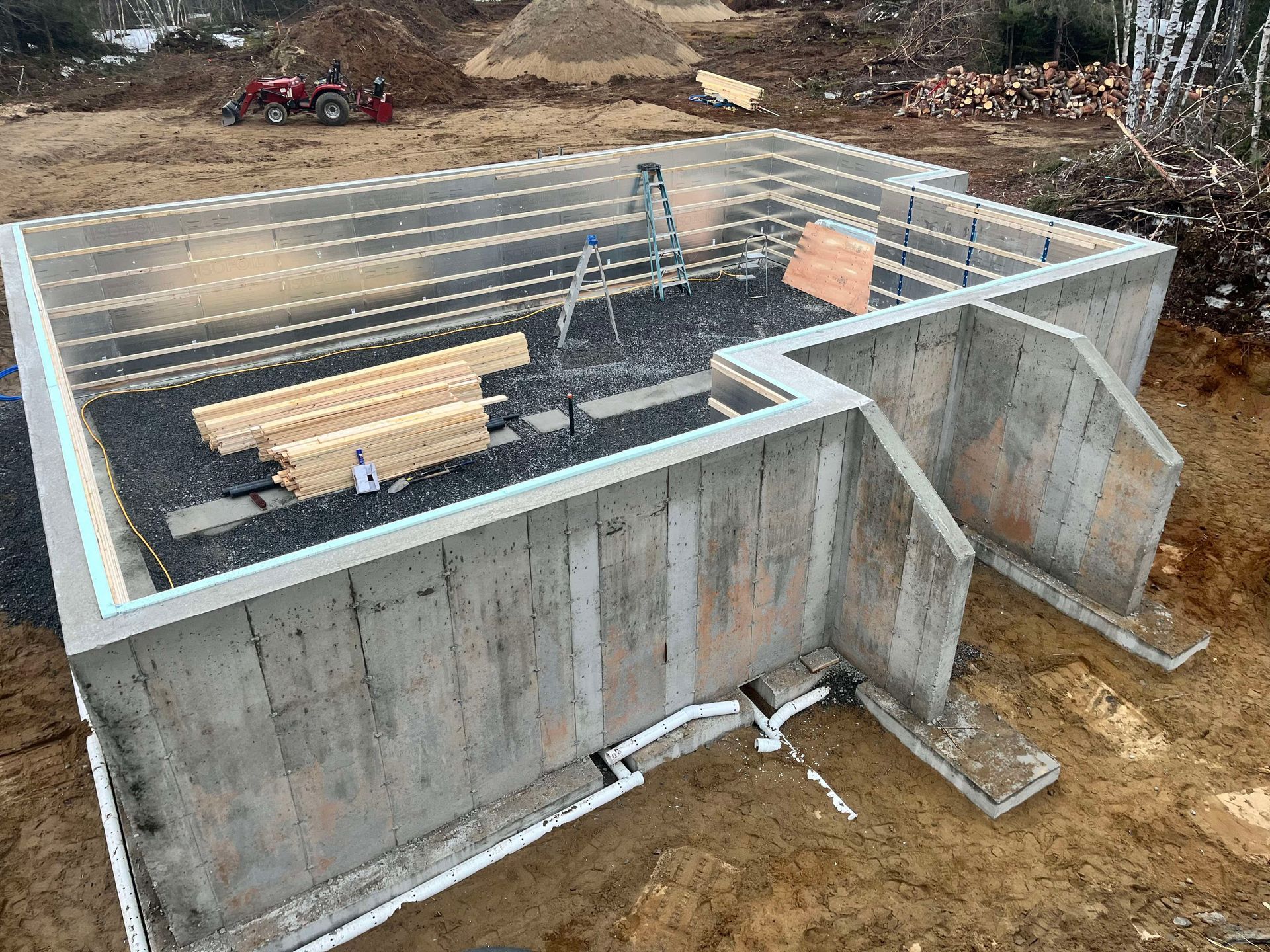 Fondations en béton en construction avec armatures, coffrages en bois et terre autour du site.