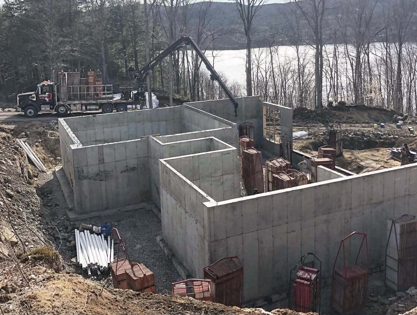 Murs de fondation en béton sur un chantier de construction avec une excavatrice et des piles de briques en arrière-plan