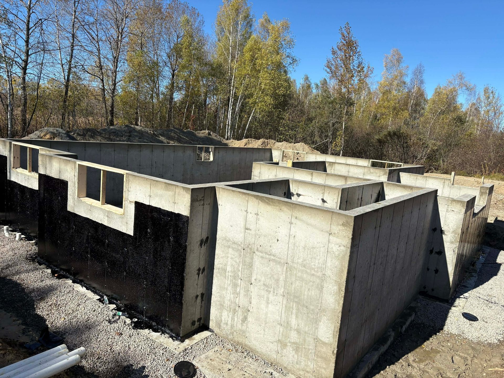 Murs de fondation en béton d'un terrain inachevé, avec des arbres et un ciel bleu en arrière-plan.