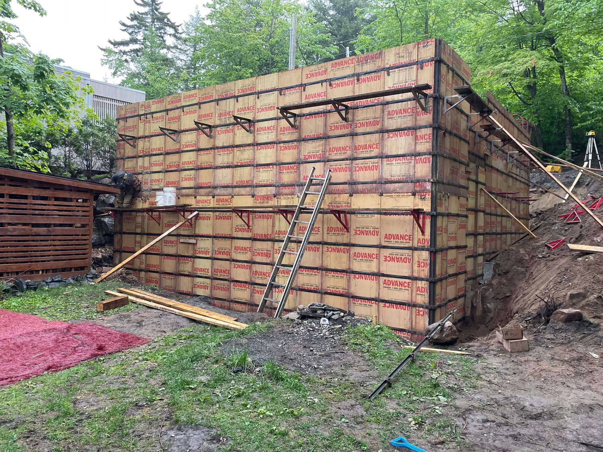 Grand mur de soutènement en béton en construction avec coffrage en bois et étais de soutien sur un site boisé