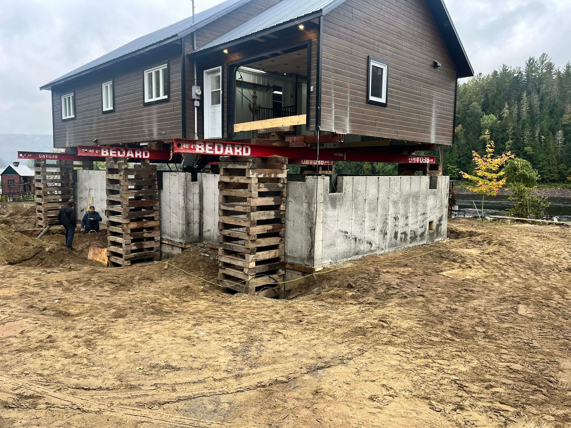 Maison soulevée par des vérins temporaires au-dessus de fondations en béton sur un chantier boueux