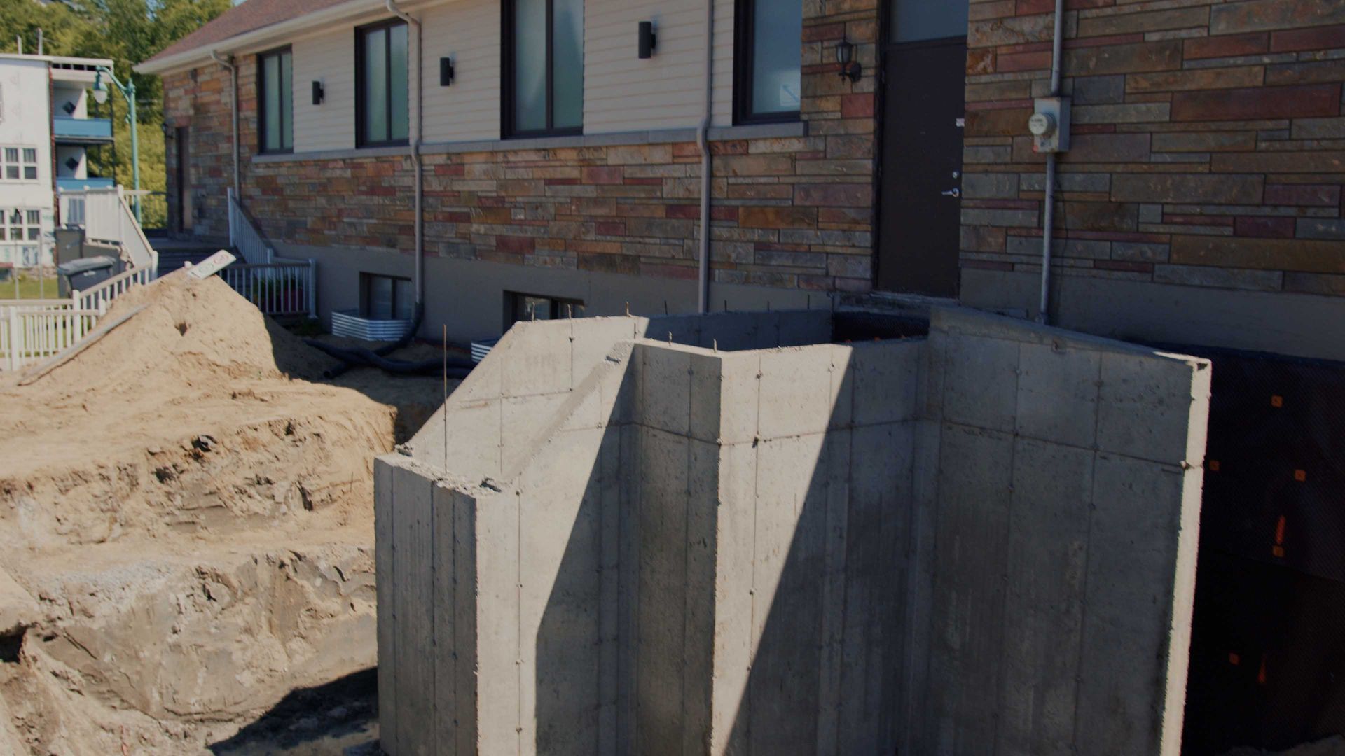 Murs de fondation en béton sur un chantier de construction résidentielle, à côté d'un bâtiment en briques.