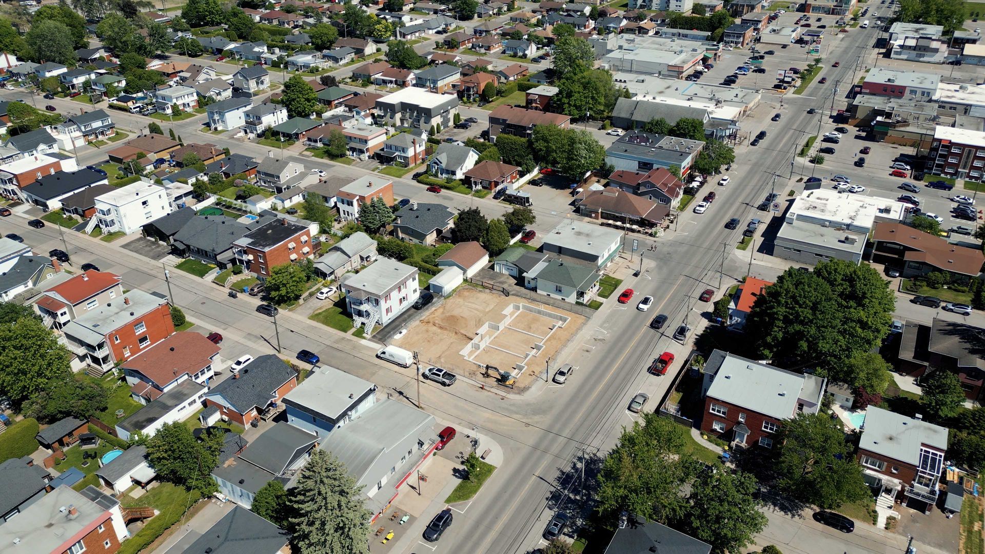 Vue aérienne d'un quartier résidentiel avec des maisons, des rues, des voitures garées et un terrain de construction.