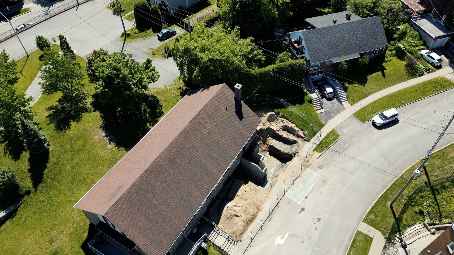 Vue aérienne d'une maison avec toiture endommagée et des débris, située au bord d'une rue résidentielle sinueuse.