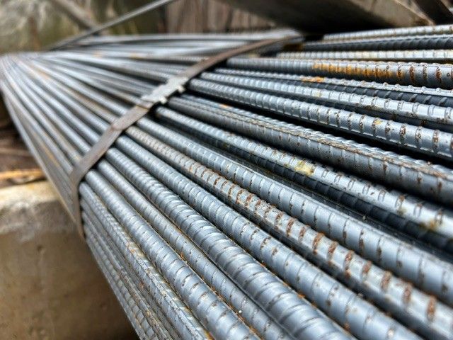 Gros plan sur un chantier de construction : barres d'armature en acier empilées et regroupées en faisceaux.