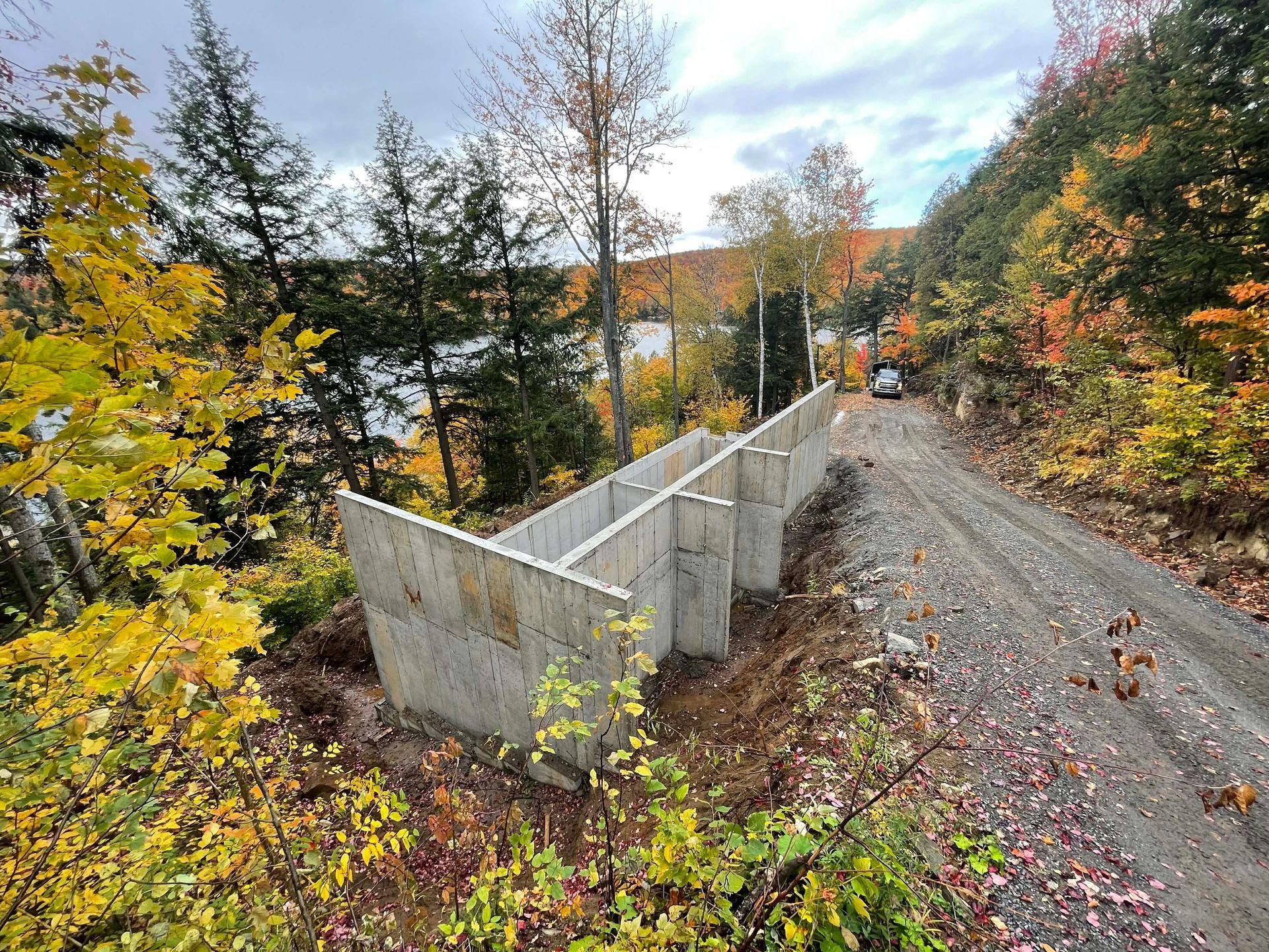 Barrière de route en béton au bord d'un chemin de gravier dans une forêt aux couleurs automnales.