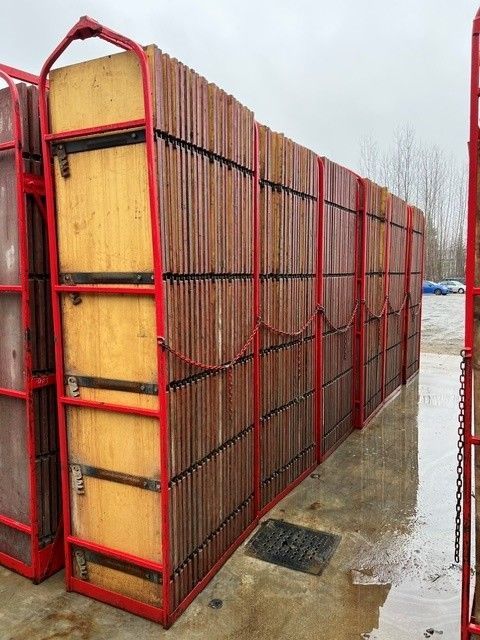 Des caisses de fret en bois à armature métallique rouge sont empilées à l'extérieur sur une surface en béton humide.