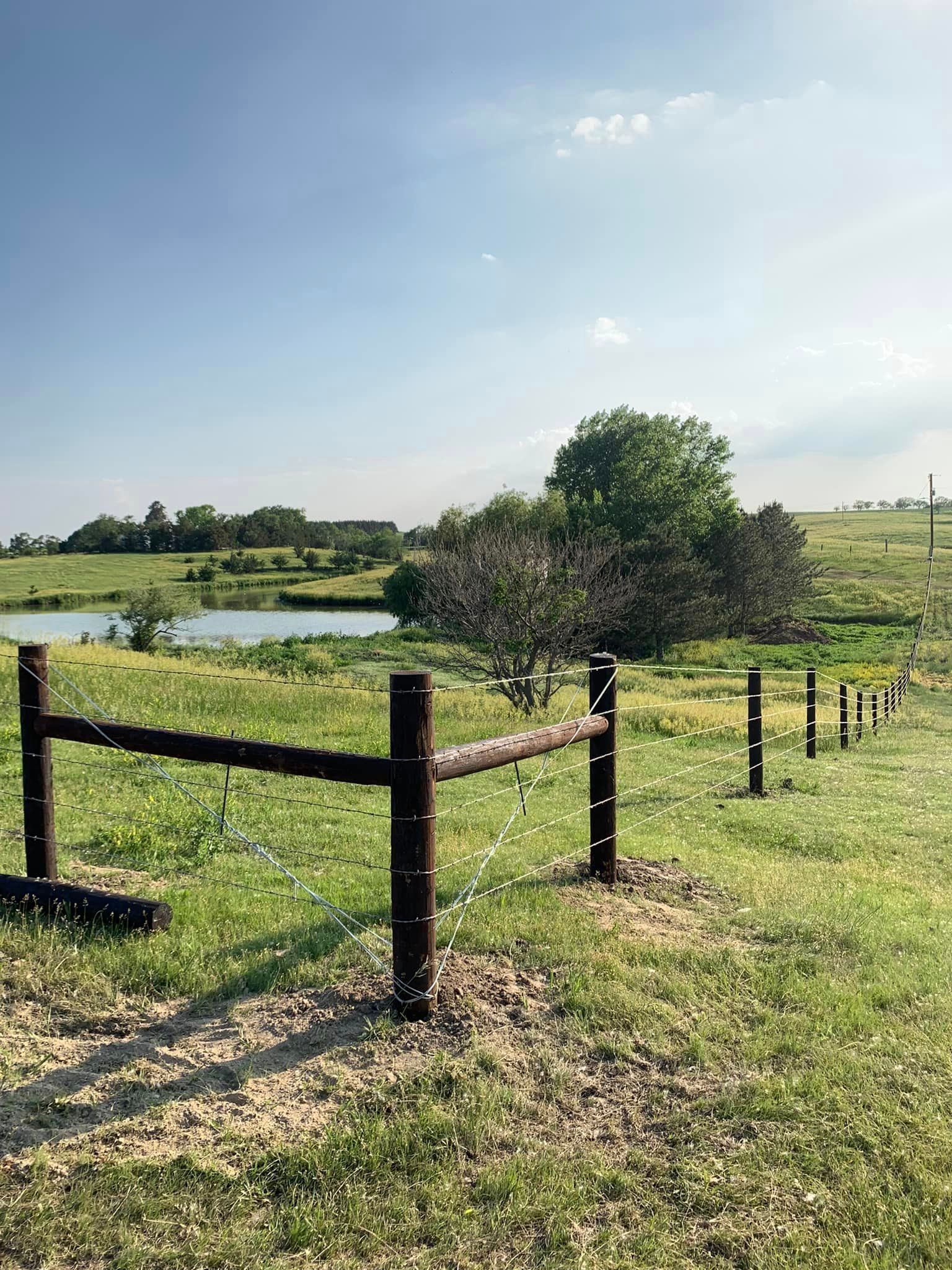 A wooden fence surrounds a grassy field with a lake in the background.