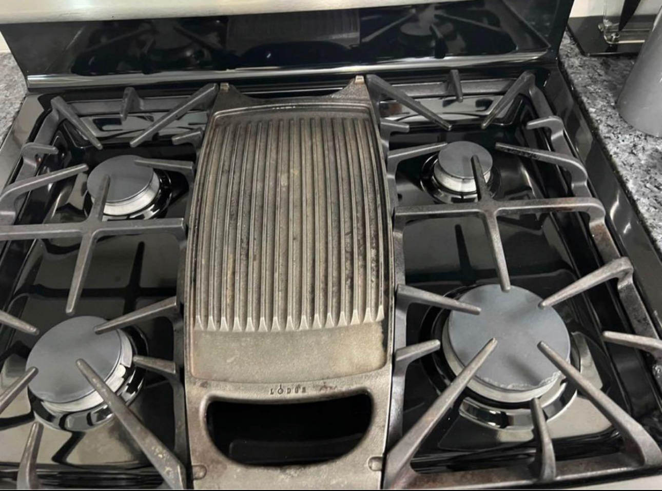 Black gas stove with four burners and stainless steel top.