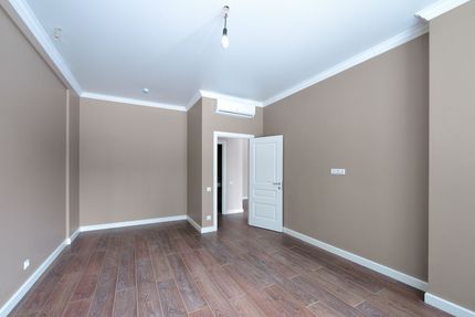 Empty room with brown walls, white trim, and a dark wood floor. A doorway is open.
