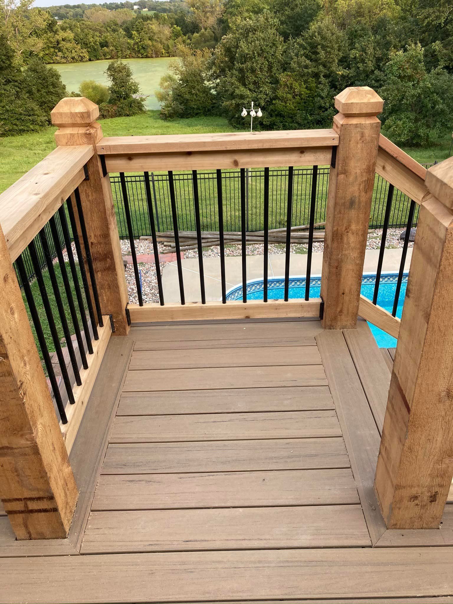 A wooden deck with a metal railing and a pool in the background.