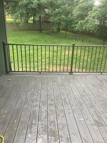 Deck with black railing overlooking a green yard, trees, and sky.