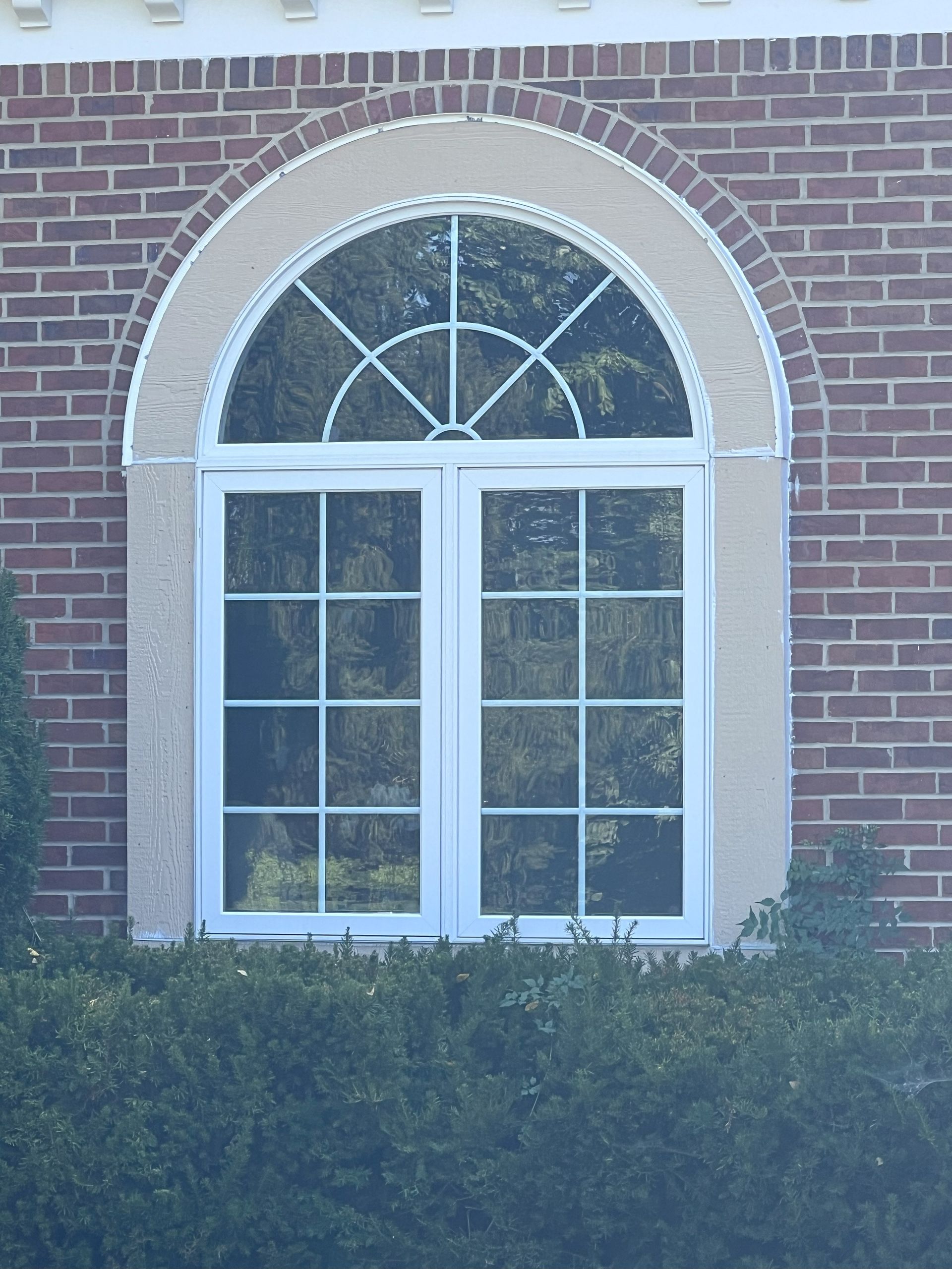 White-framed arched window with mullions, set in a brick wall with beige trim.