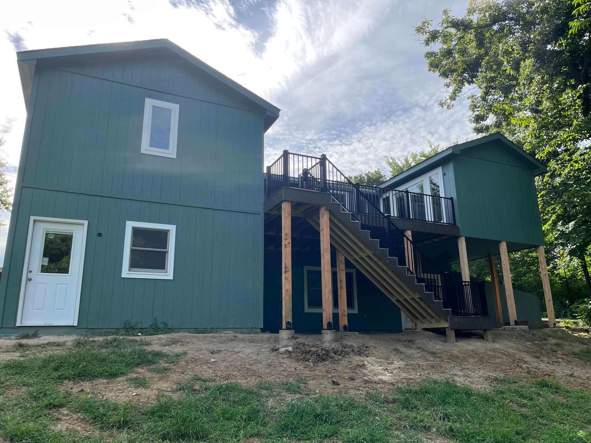 Green house with deck and stairs; cloudy sky overhead.