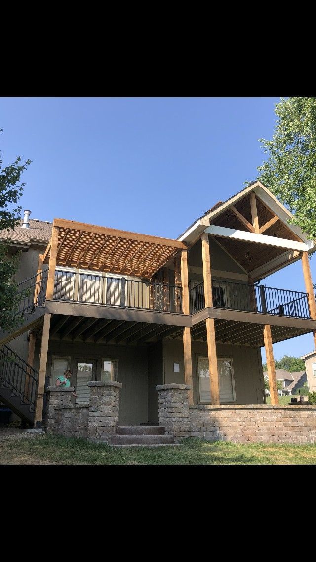 Two-story house with wooden deck and pergola, against a blue sky.