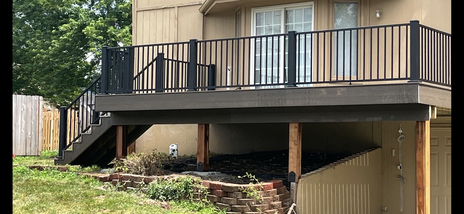 A composite deck with black railings and stairs. Brown wooden support beams are visible.