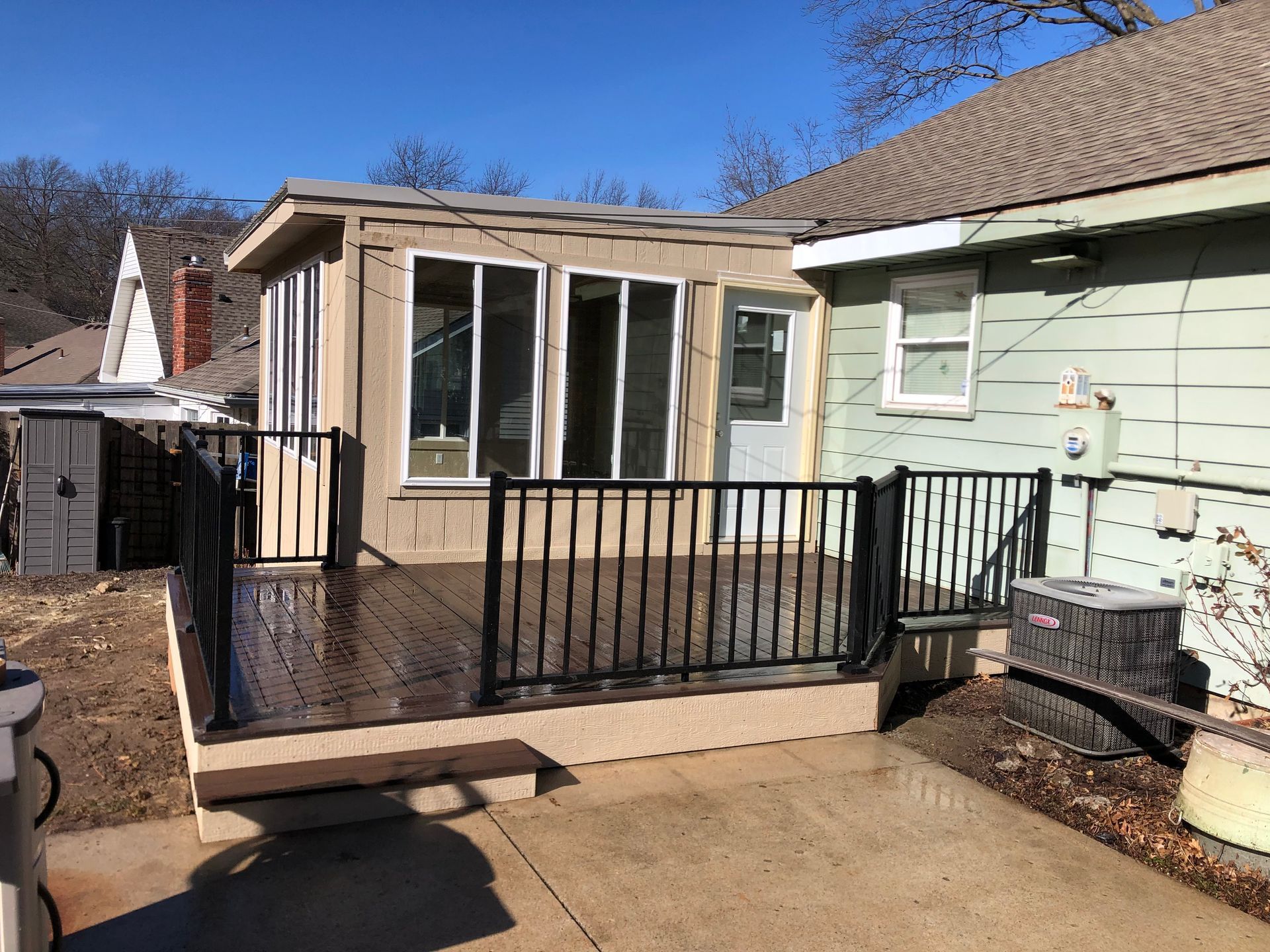 Backyard deck with black railing and enclosed sunroom, next to a light green house.