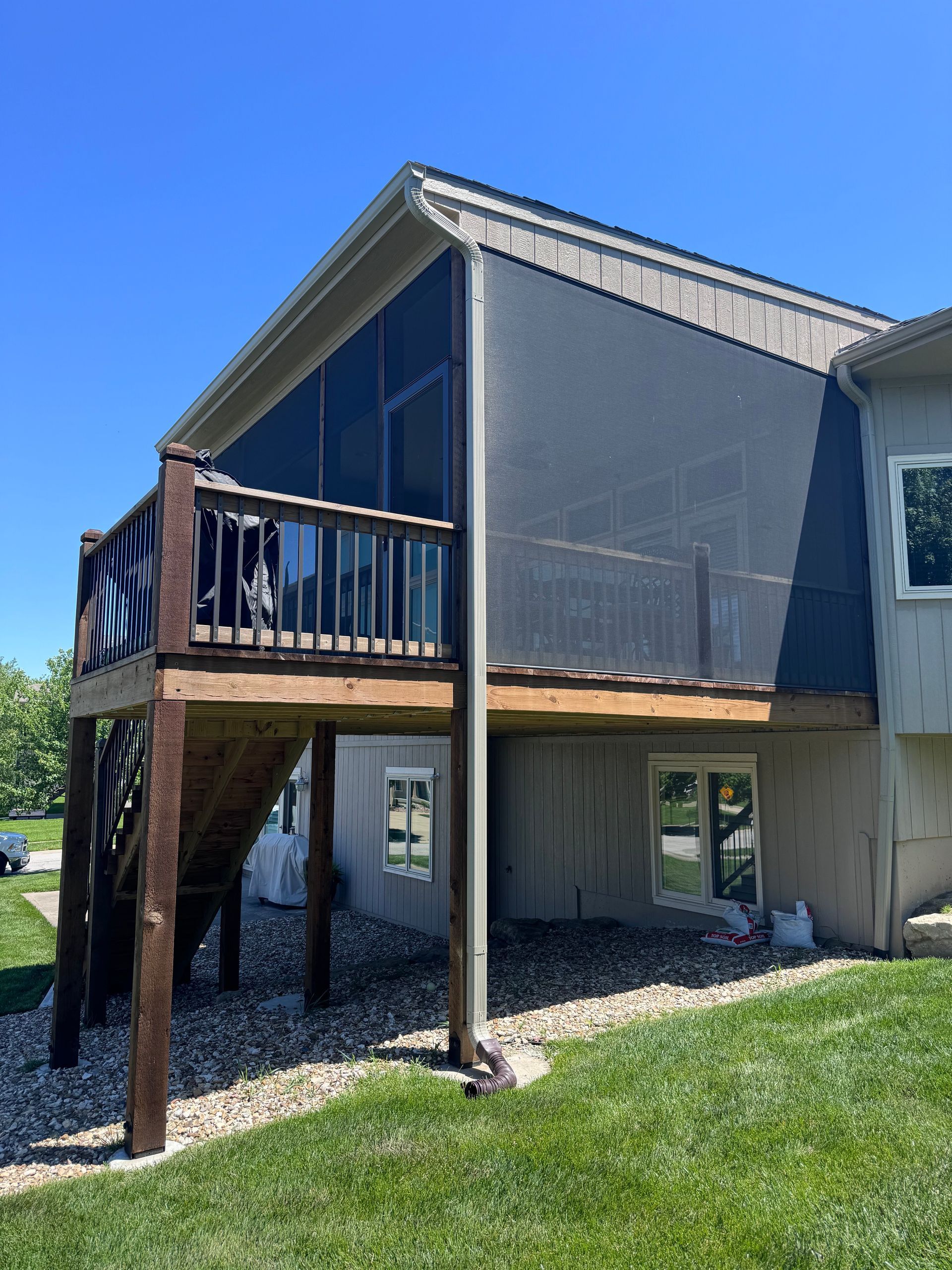 Deck with screened enclosure, attached to a house with beige siding, on a sunny day.