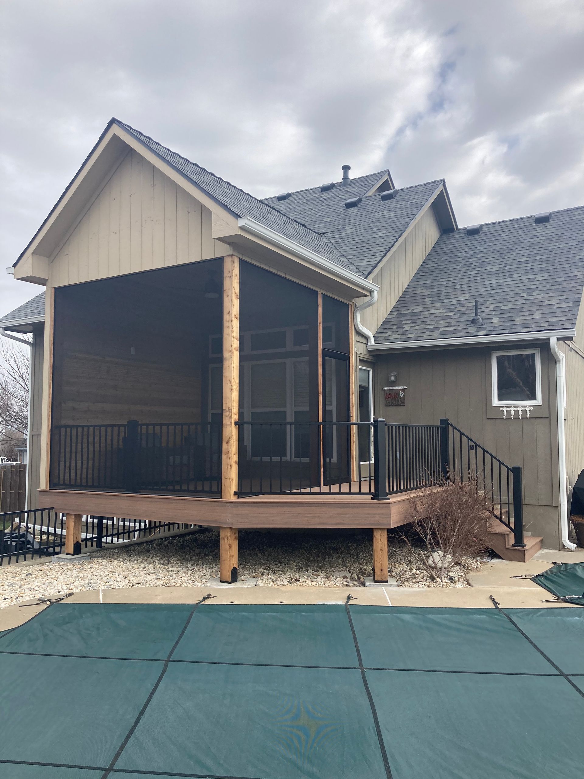 Screened-in porch and deck attached to a house with a pool cover in the foreground.