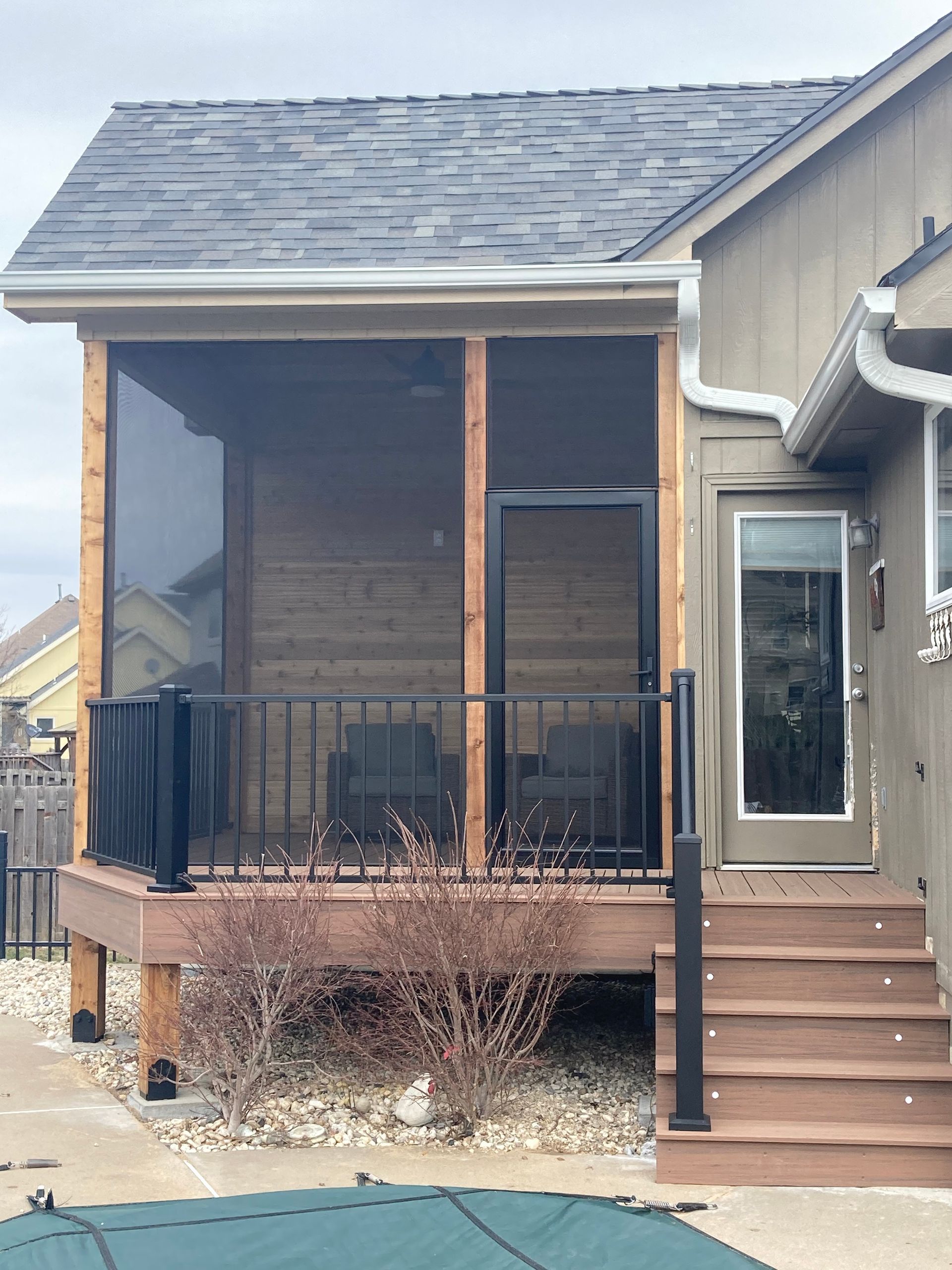 Screened-in porch addition with black railing and door. Steps lead to a door on the right side.