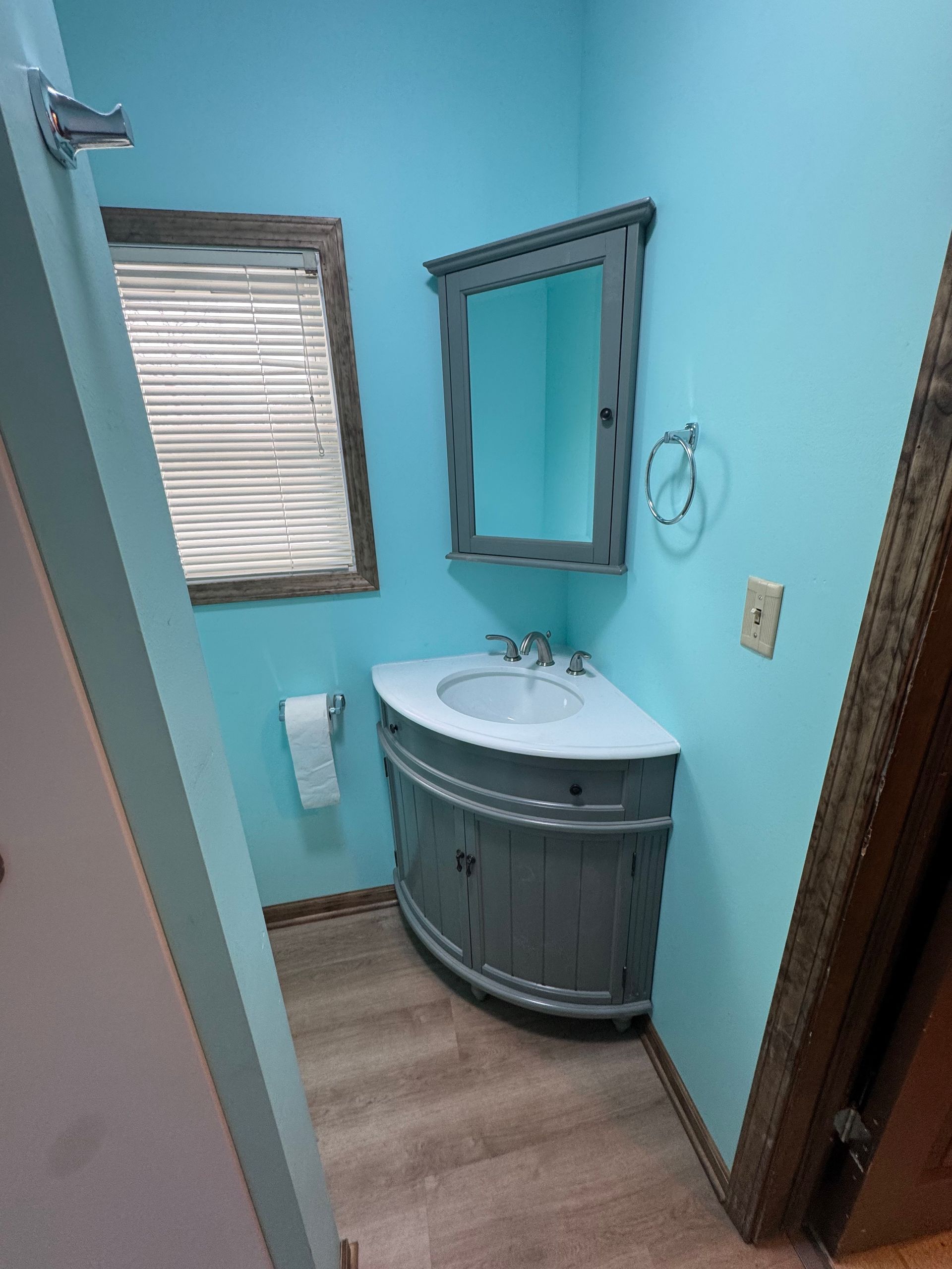 Small bathroom with blue walls and a gray vanity, mirror, and cabinet.