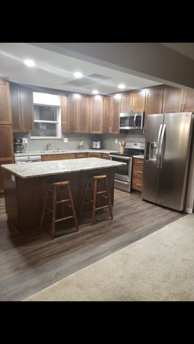 Kitchen with brown cabinets, stainless steel appliances, and island with bar stools.