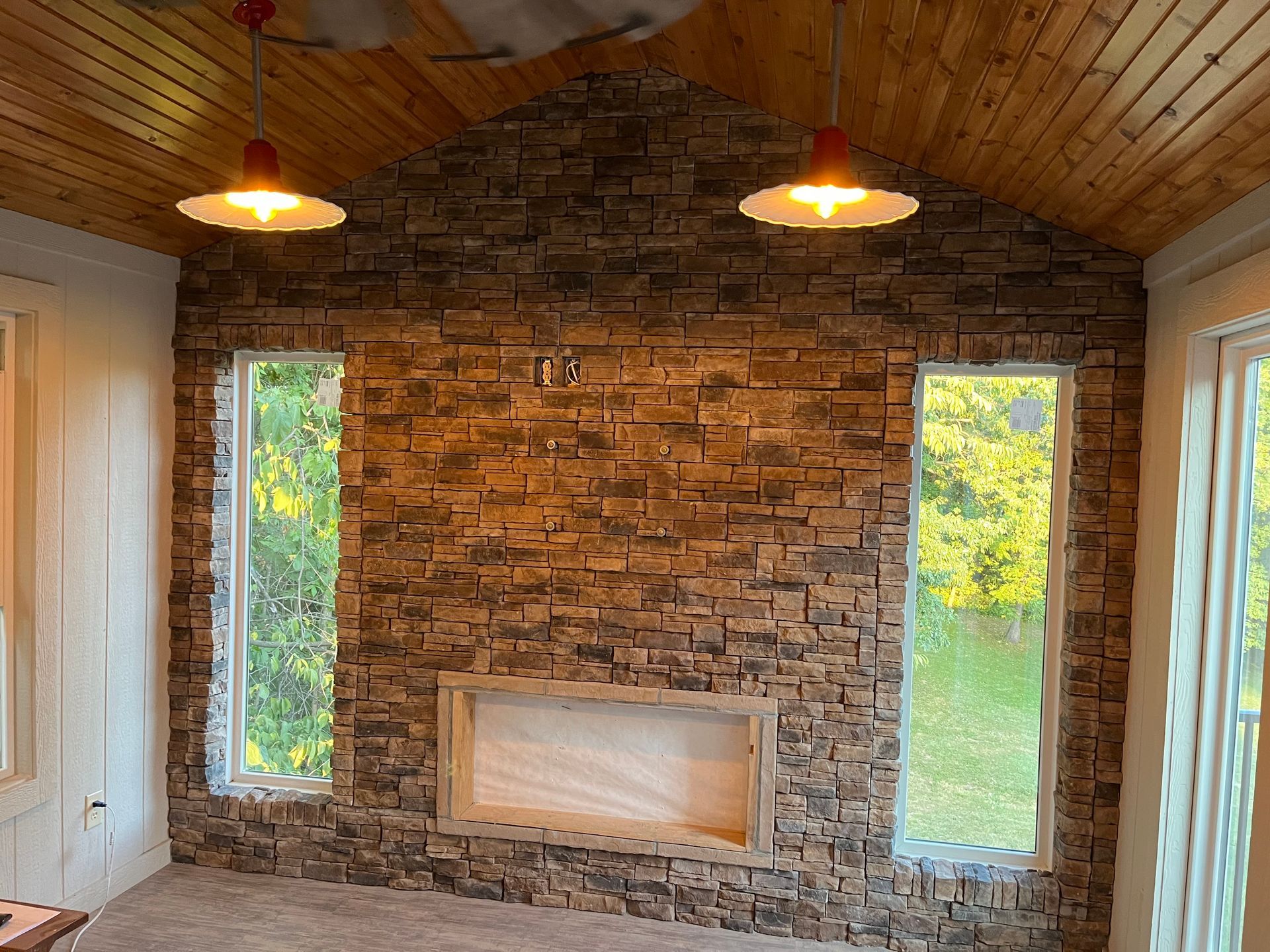 Stone accent wall with two windows, a fireplace opening, and pendant lights.