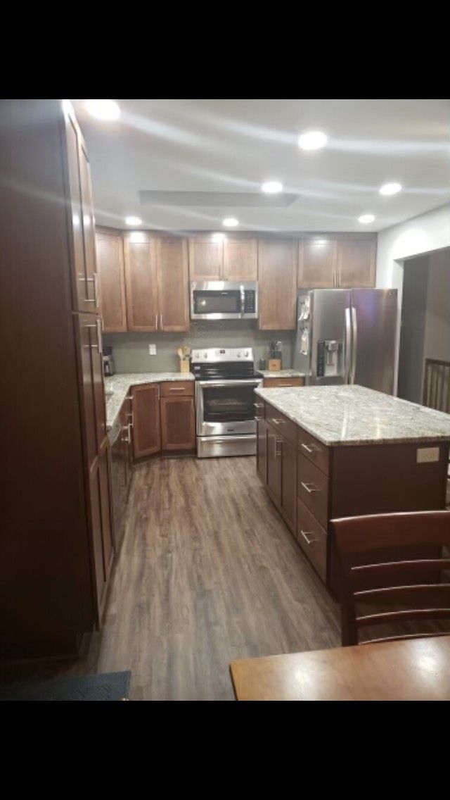 Brown kitchen with island, stainless steel appliances, granite countertops, and wood flooring.
