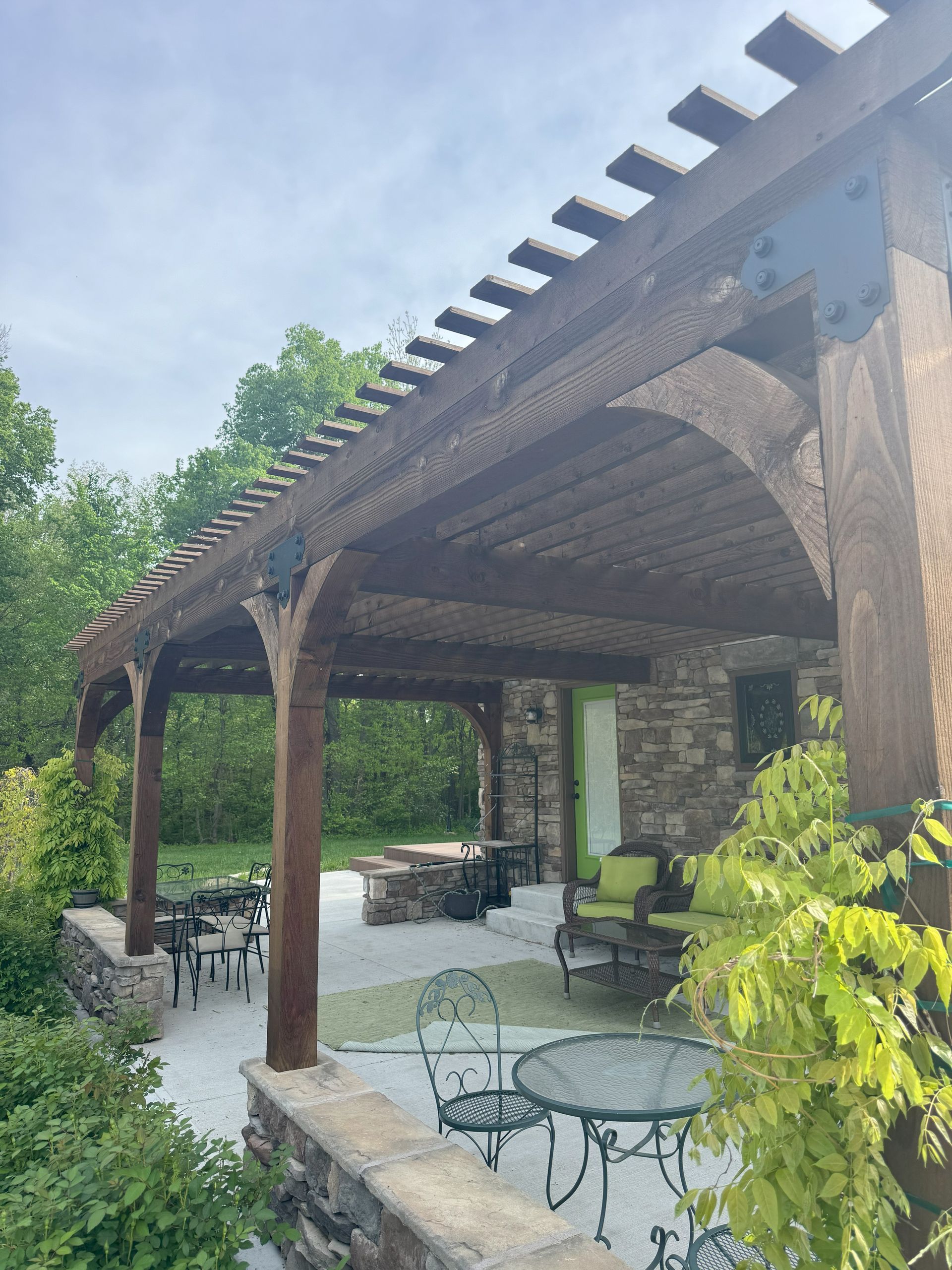 Wooden pergola over patio with seating and stone wall, outdoors.