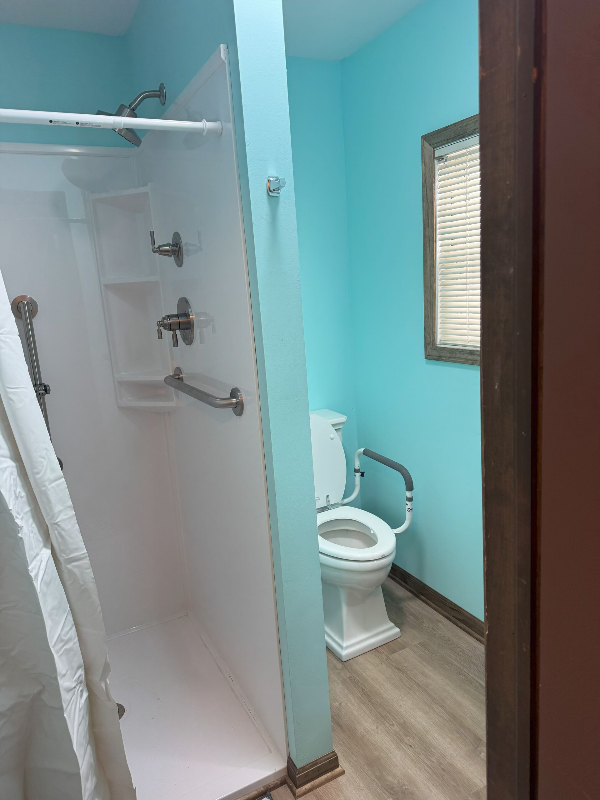 Accessible bathroom with a white shower, toilet with grab bars, and blue walls.