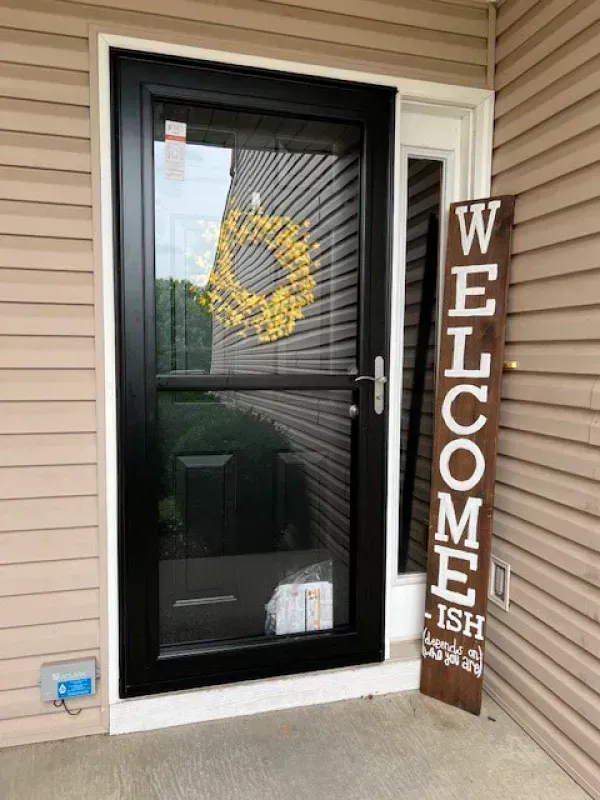 A black door with a wreath on it and a welcome sign