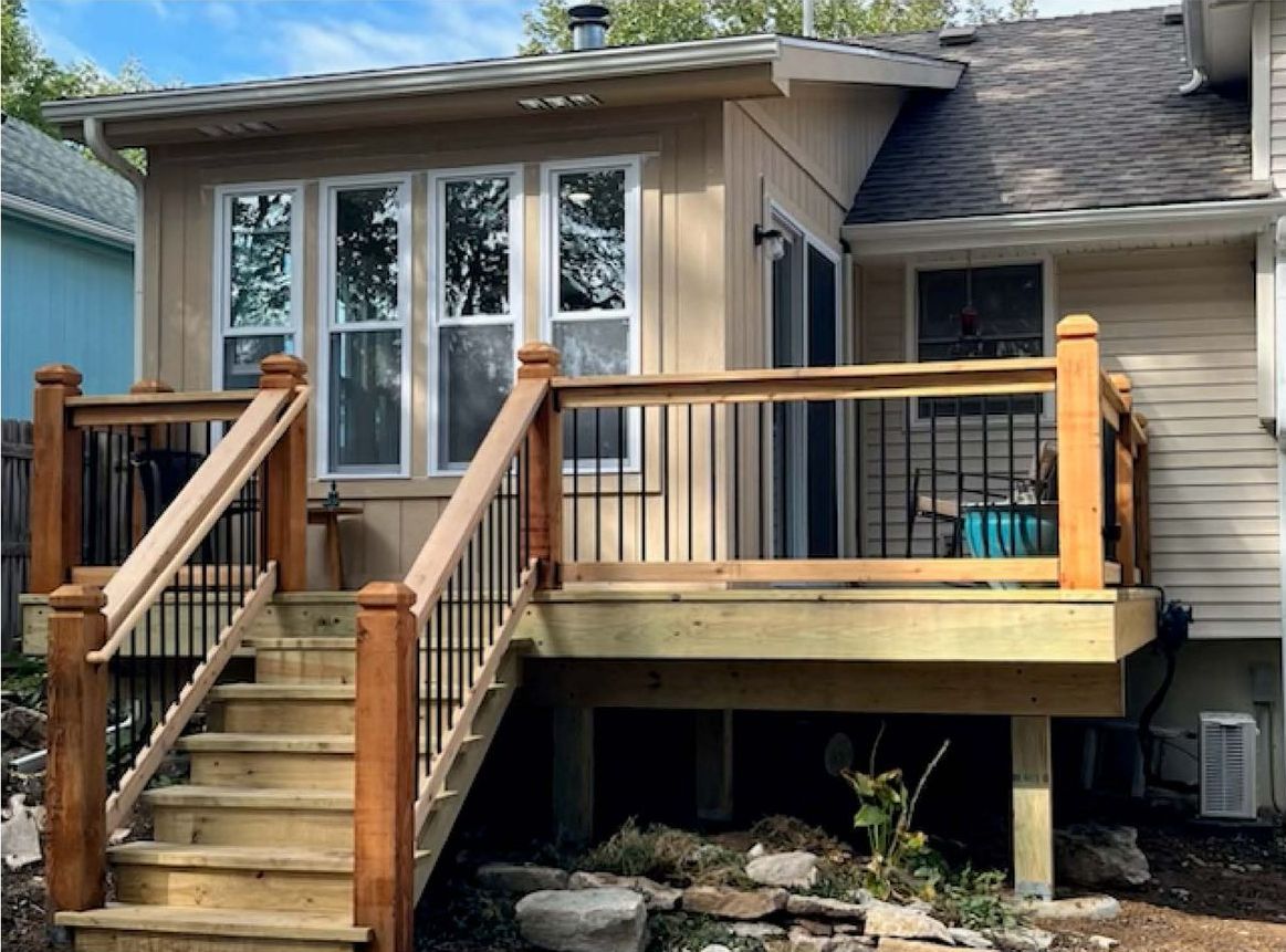 Wooden deck with stairs, black railing, and beige house with windows.