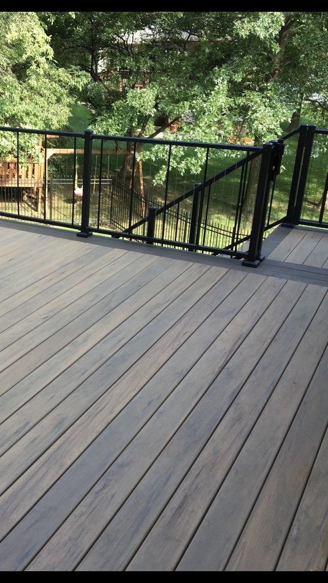 Wooden deck overlooking a calm body of water, surrounded by trees and a black railing.