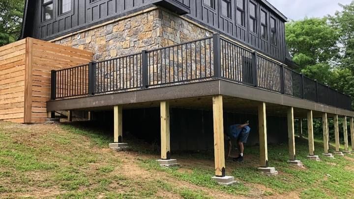 Wooden deck on a hillside house with dark railings and a person working underneath.