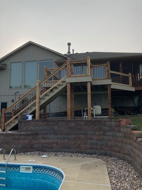 Deck with stairs, overlooking a pool, built into a retaining wall, attached to a house.