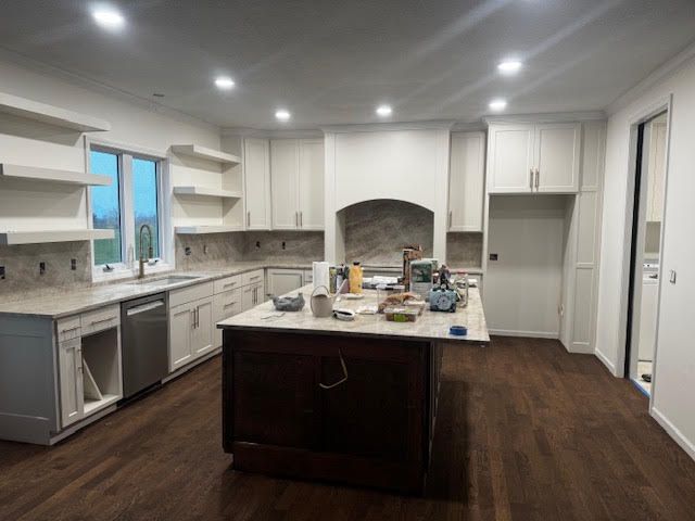 Renovated kitchen with light cabinets, dark island, and hardwood floors. Construction tools on island.