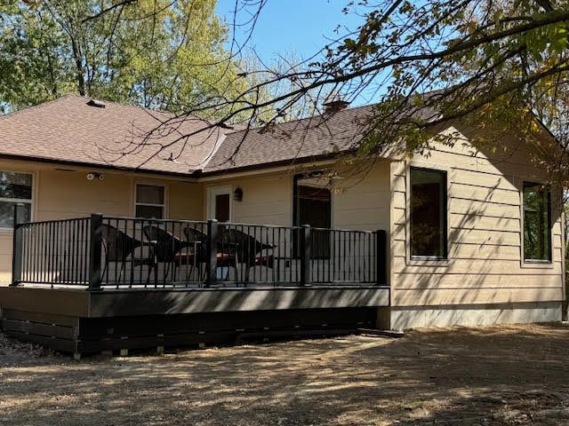A beige house with a brown roof and a wooden deck with black railings.