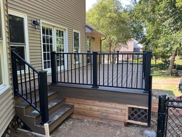 Backyard composite deck with black railings and steps, built on a home with tan siding.