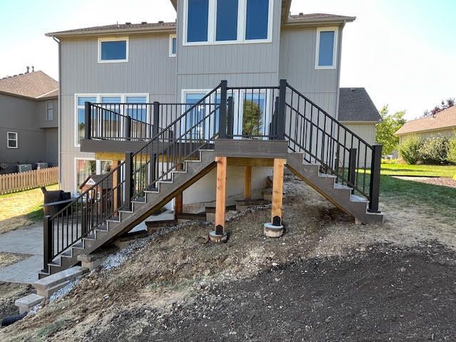 Multi-level deck with black railings and stairs on a sloped yard against a two-story gray house.